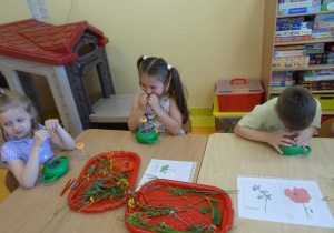 Dzieci obserwują rośliny, wąchają w sali przedszkolnej.
